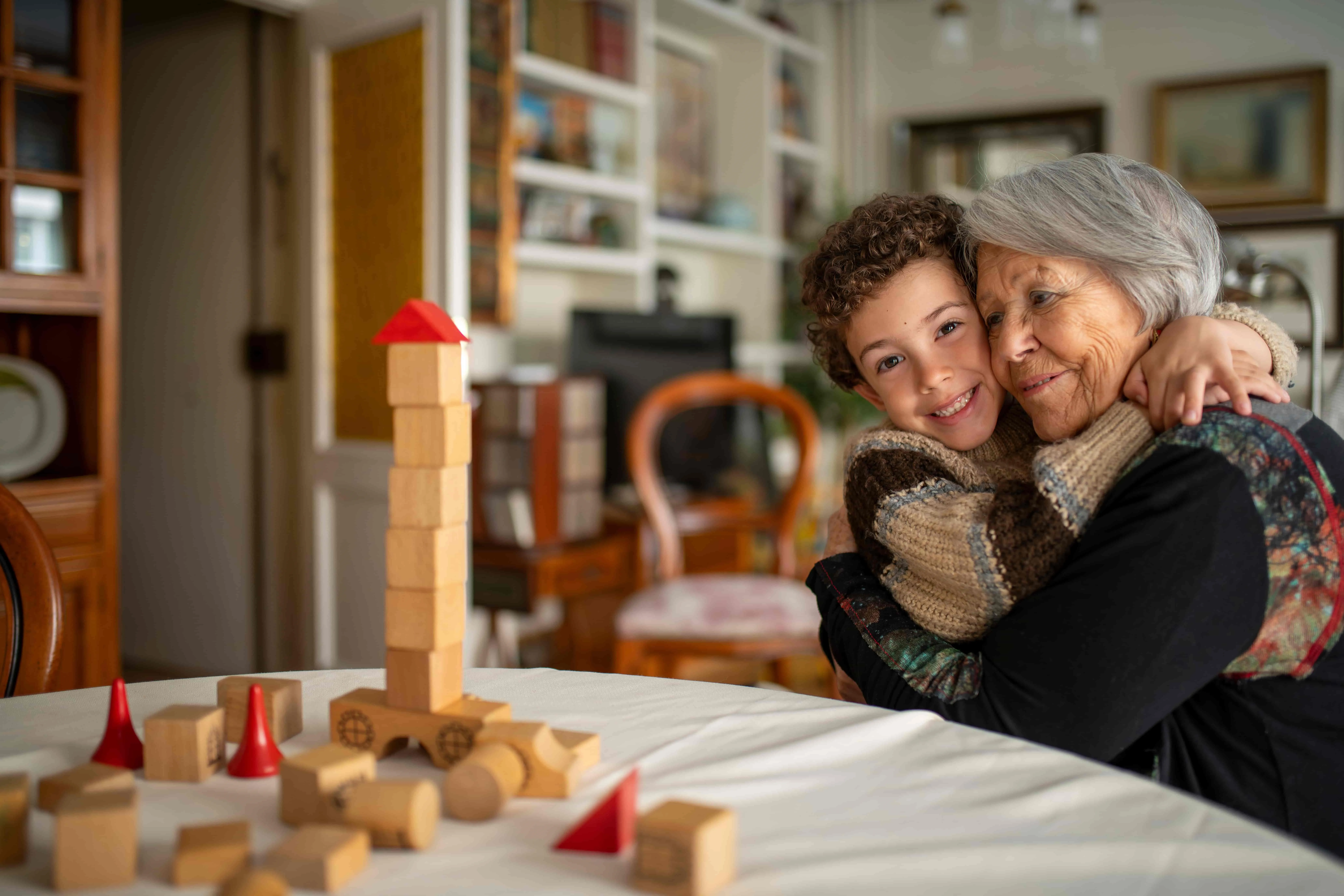 Grandchild hugging grandmother at home playing with wooden toys